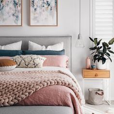 a bed with pink and grey sheets in a bedroom next to two pictures on the wall