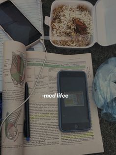 an open book and cell phone on the ground next to other items that include food