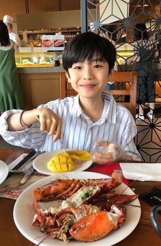 a young boy sitting at a table with lobsters and chips in front of him