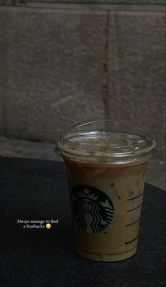 a cup of iced coffee sitting on top of a table next to a brick wall