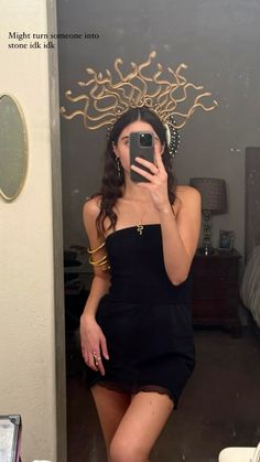 a woman taking a selfie in a mirror wearing a black dress and gold jewelry