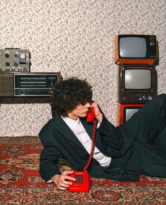 a man sitting on the floor talking on a red telephone