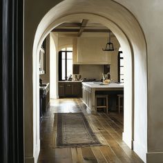 an archway leading into a kitchen with wooden floors and white walls, along with a rug on the floor