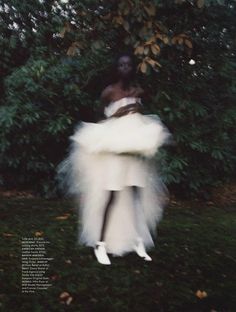 a woman is standing in the grass with her arms around her body, wearing a white tutu skirt