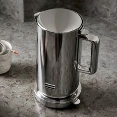 a silver coffee pot sitting on top of a counter next to a cup and saucer