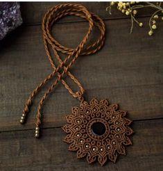 a brown necklace with a black stone in the center on a wooden table next to some flowers