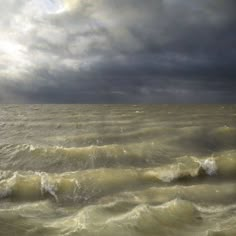 the ocean is very choppy and dark with some clouds in the sky above it