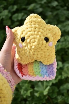 a person holding up a crocheted stuffed animal in front of some bushes and trees