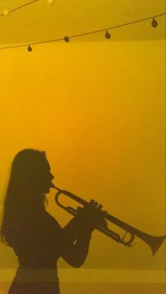 a woman holding a trumpet in front of a yellow wall with string lights on it