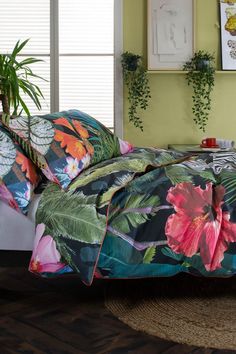 a bed covered in a floral comforter next to a window with potted plants