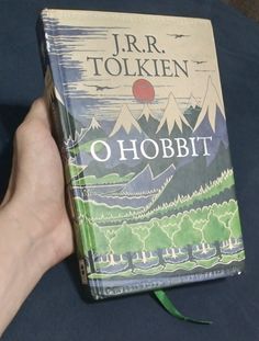 a hand holding a book in front of a blue tablecloth with mountains and trees on it