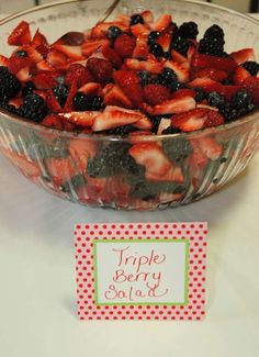 a bowl filled with strawberries and blackberries next to a sign that says triple berry salad