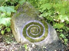 a rock with a spiral design on it in the grass next to some trees and bushes