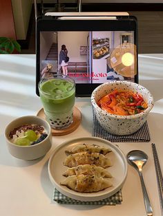 a table topped with plates and bowls filled with food next to a tablet computer screen