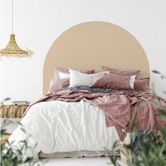 a bed with pink and white linens in a bedroom next to potted plants