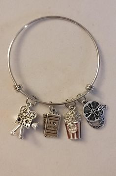 Silver Movie Lover Bangle Bracelet comes with all 4 charms shown. Bracelet is stainless steel and charms are of various different metals.  To personalize your bracelet please look in our "ADD ON" section.  There you will find birthstones,  initials and much more that you can add to your bracelet to personalize it.  To get to out ADD ON section just go to our homepage (Charming Julz) and in the search bar at the top of the page you can type ADD ON and hit enter.  This will land you on all of our Add on items. If you find something you would like simply add it to your cart (along with this bracelet)  Once you have everything you want in your cart you can select purchase to purchase everything . Please feel free to message us with any questions you may have.  Thank you so much. Gift For Movie Lover, Charmed Show, Movie Buff, Search Bar, Movie Lover, The Search, Charm Bracelets, Bracelet Gift, Bangle Bracelet