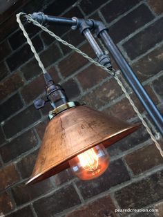 a light hanging from the side of a brick wall next to a metal pipe and lamp