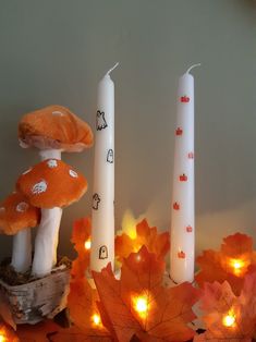 three candles with mushrooms on them are sitting in front of some autumn leaves and lights