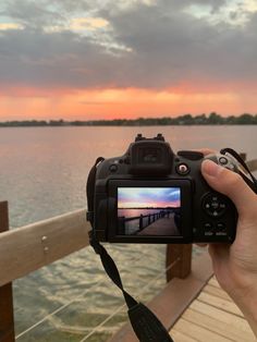 a person holding up a camera to take a photo near the water at sunset or dawn