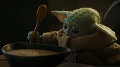 the child yoda doll is holding a spoon in its hand and stirring it into a bowl