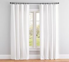 a white curtain hanging in front of a window next to a wooden floor and wall