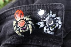 two spider brooches sitting on the back of a pair of black jean pants