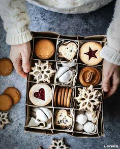 a person holding a box filled with different types of cookies and pastries on top of a table