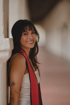 a woman leaning against a wall wearing a red and black neck tie with tattoos on her arm