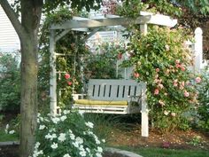 a white bench sitting under a tree next to flowers