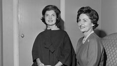 two women standing next to each other in front of a door wearing dresses and pearls