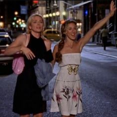 two women are standing on the street waving