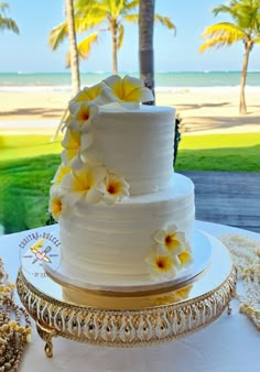 a white wedding cake with yellow flowers sitting on top of a table next to the ocean