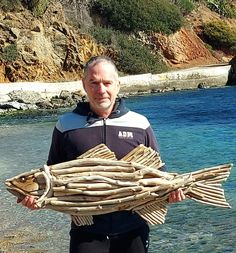 a man standing in the water holding a large fish made out of driftwood sticks