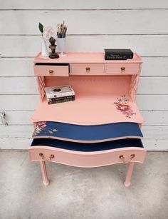 a pink desk with three drawers and two books on top, next to a white wall