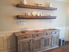 two wooden shelves above a buffet with dishes on it and wine glasses on the top shelf