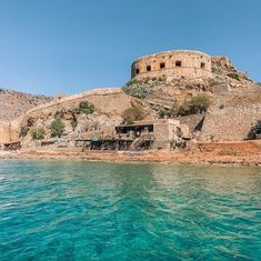 an old stone building on top of a hill next to the ocean with clear blue water