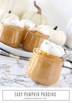 two pumpkin puddings with whipped cream on top in small glass jars next to white pumpkins