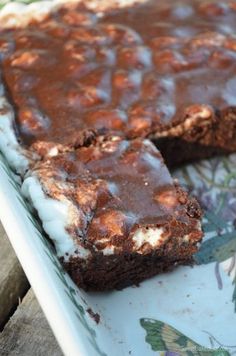 a chocolate cake with white frosting sitting on top of a floral table cloth next to a slice cut out of it