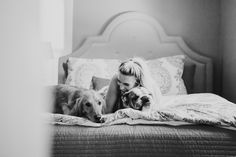 a woman laying on top of a bed with two dogs next to her in black and white