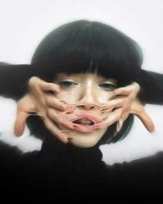 a woman with black hair covering her face and hands behind her head, posing for the camera