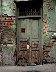 an old building with two green doors and rusted iron bars on the front door