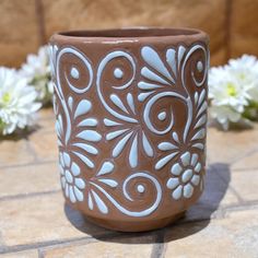 a brown and white flower pot sitting on top of a tile floor next to flowers