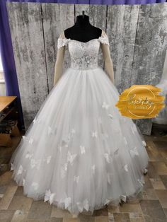 a white wedding dress with butterflies on the skirt and off the shoulder, sitting on a mannequin