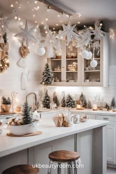 a white kitchen decorated for christmas with lights and decorations on the counter top, along with evergreen trees