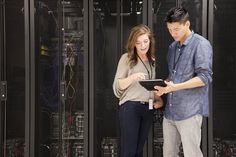 a man and woman standing in front of server racks looking at something on a tablet