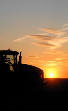 the sun is setting behind a tractor in the middle of an open field with clouds