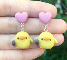 two little yellow birds with pink hearts hanging from them's earring hooks in their hand