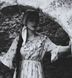 black and white photograph of woman in dress standing next to large rock with open arms