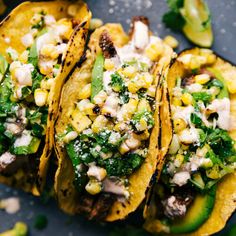 three tacos with corn, avocado and feta cheese on them sitting on a plate