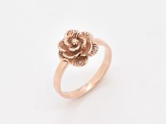 a gold ring with a rose on the front and center, sitting on a white surface